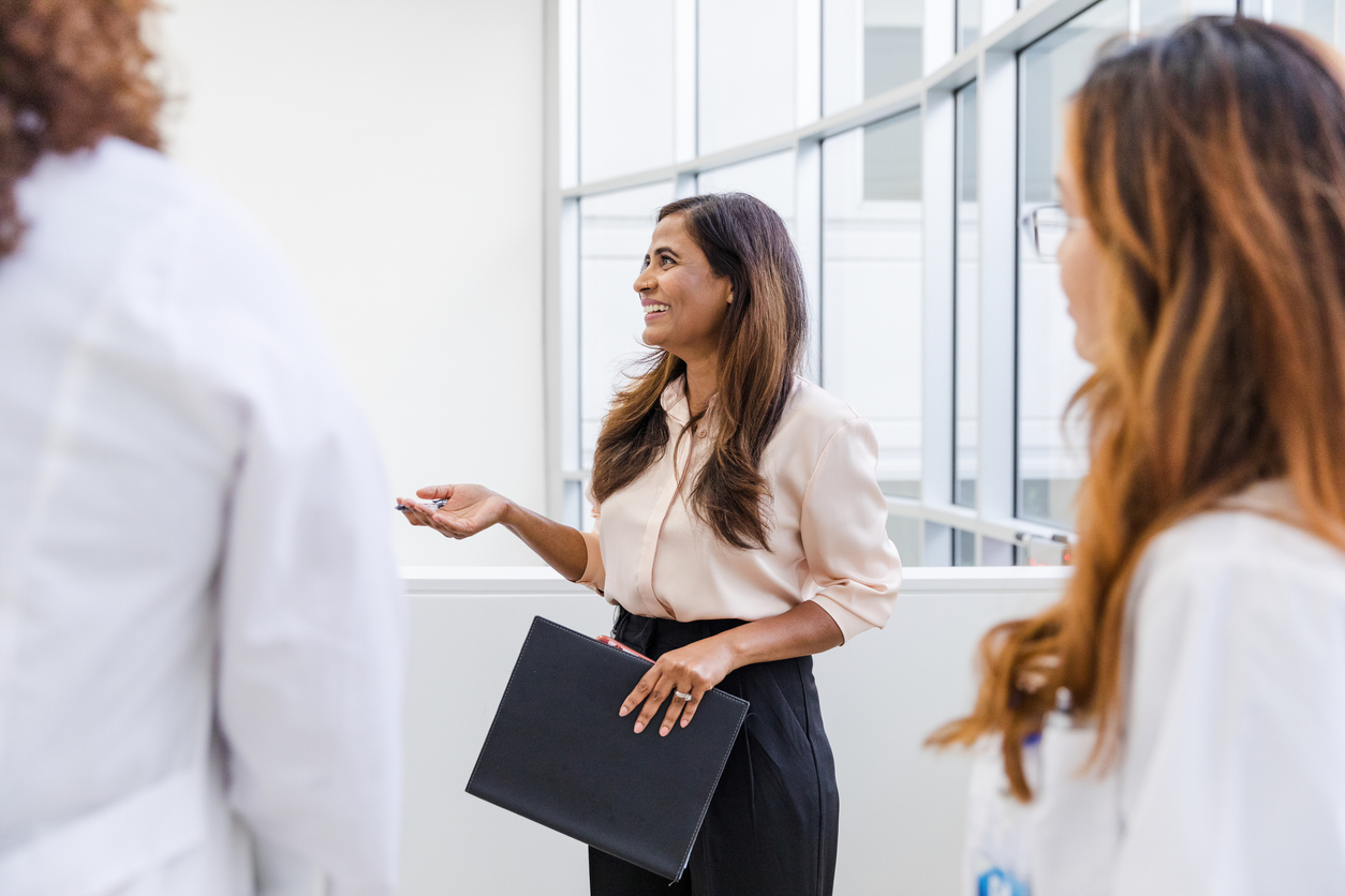 A health care manager talks with clinicians in a hospital corridor.