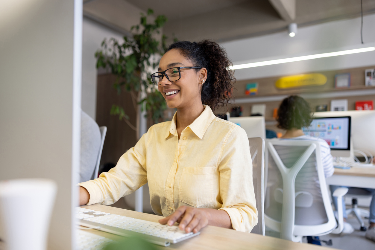 A smiling supply chain manager works on a computer in an office.